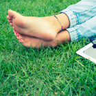 Woman&#039;s Feet In The Grass Next To A Cell Phone And Laptop