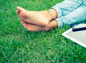 Woman&#039;s Feet In The Grass Next To A Cell Phone And Laptop