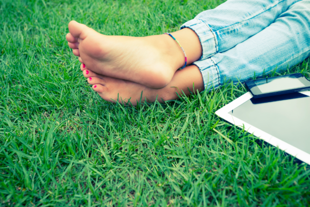 Woman&#039;s Feet In The Grass Next To A Cell Phone And Laptop